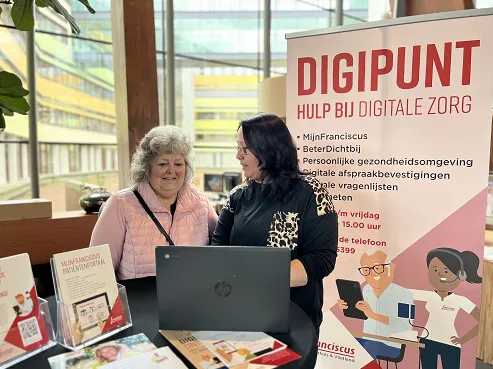 Medewerker van het Digipunt helpt een patiënt met digitale zorg bij een informatiestand in het ziekenhuis. 